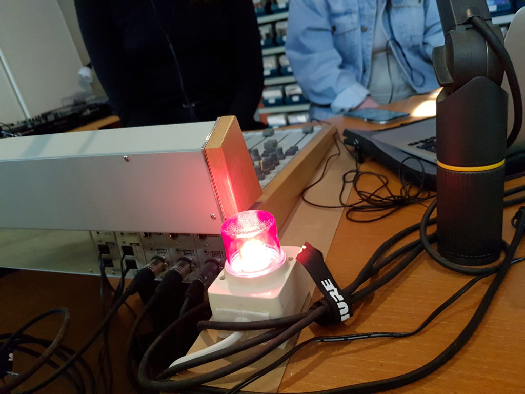 På bilden syns ett mixerbord och en rött lysande lampa som visar att inspelning pågår. I bakgrunden ser man Tilda och Wendela.